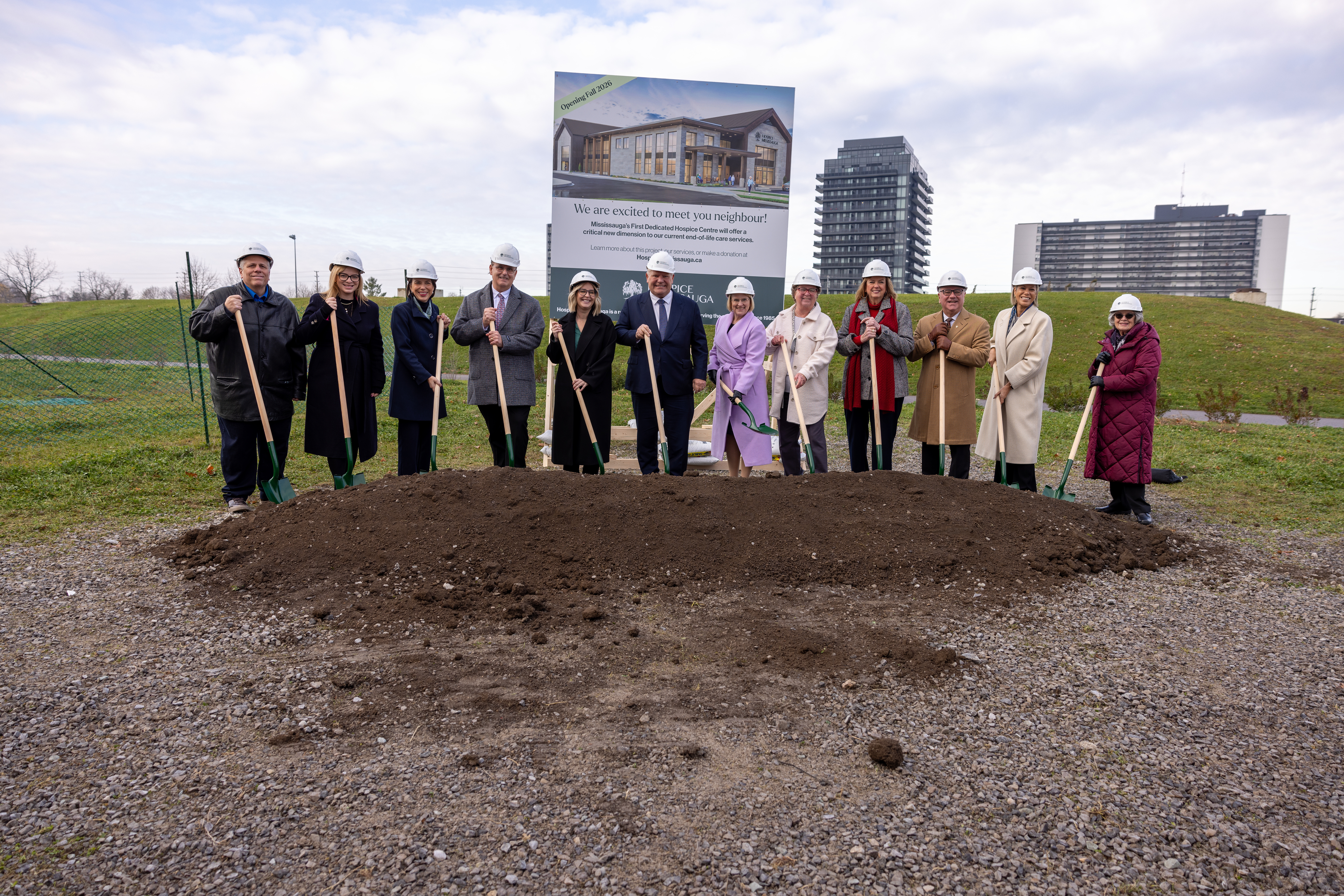 Group of men and women with shovels in a field posing for a picture and breaking ground on a new hospice centre