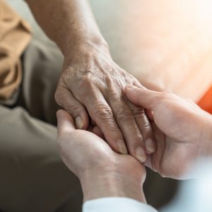 The hand of a senior being held by the hands of a middle-aged person